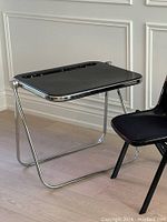 Front view of Platone folding desk with black top and chrome tubular frame.