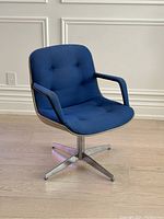 Front angle showing entire chair with blue tufted upholstery, chrome base, and cream shell