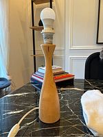 Front view of vintage IKEA LÄNS lamp with turned beech wood base sitting on black marble table. Lamp has natural wood finish and white LED bulb installed, cord and inline switch visible.