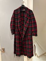 Full view of the vintage Pendleton wool housecoat hanging on door showing red and black plaid pattern, buttons, pockets, and belt.