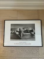 Full view of the framed black and white male nude print poster by Naomi Stanley titled Portfolio Gallery lying on a light wood floor.