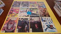Photo showing all 12 comics laid out on a yellow table including 3 Planet of the Apes comics, Redblade, Encounter, and others.