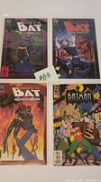 Four Batman-related comic books in protective sleeves, arranged on a white surface, showcasing their front covers including three 'Shadow of the Bat' comics and one with classic Batman villains.