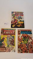 Three Bronze Age comics shown: Giant Size Iron Man #1 with a Marvel heroic cover and two other comics Chamber of Chills #22 and The Defenders #80 with vintage colorful covers, placed flat with price tag visible on first comic.