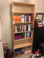 Full view of tall faux wood bookcase with five shelves filled with books and games to show shelving size and capacity.