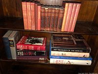 Shelf with 9 red and tan hardcover books, gold embossed titles (The Great Novelists and others) and coffee table books on lower shelf (Art Treasures of the Vatican, Poland, etc.)