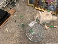 View of all items in the lot including glass cake stand with lid, large glass trifle bowl, multiple acrylic bowls, and Fitz and Floyd ceramic tureen shaped like a bird with ladle.