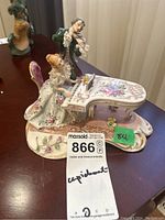 Full view of Capodimonte porcelain figurine showing couple with piano and violin, with visible damage to violin parts and lace sleeve, placed on wooden surface.