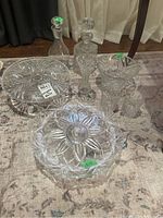 Overview of all crystal and glass items including cake stands, decanters, vase, bowl, and two glasses placed on carpeted floor.