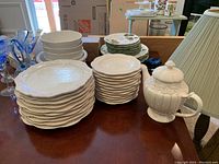 Stack of Roscher & Co Chantilly Collection dinner plates and American Atelier side plates alongside a white ornate teapot with a chipped spout.
