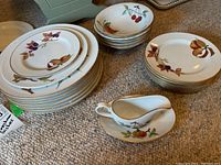 Full view of plates, bowls and creamer arranged on carpet, showing fruit motif design and condition.