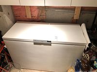 Full view of white Eaton Viking chest freezer with metal latch, placed in basement with visible items around it.