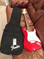 Full view of red guitar and black Fender gig bag on couch