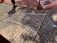 Photo of full cotton rope hammock laid out on stone patio, showing wooden spreader bars and rope netting.