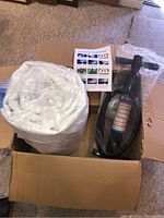 Box opened showing rolled white inflatable mat, black hand pump, and instruction manual inside