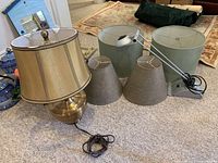 Two lamps and four lamp shades displayed on carpeted floor, showing brass base lamp, portable desk lamp, and all shades.