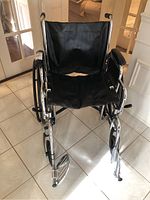 Front view of Medline manual wheelchair showing black vinyl seat and footrests on tile floor indoors.