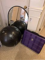 Photo showing two large black exercise balls, purple plastic case with plaid pattern on carpet near a white door