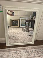 Mirror photographed upright with visible white textured composite frame and reflective surface showing room and pictures behind.