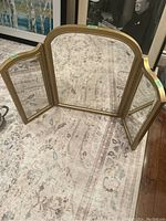 Image showing the trifold mirror fully open on carpet, central arched mirror with two side rectangular mirrors hinged to fold inward.