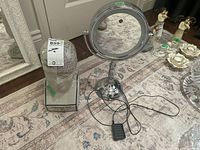 Both items visible on a patterned rug near a door: the light up magnifying mirror with cord and foot pedal and the phrenology head on rectangular base.