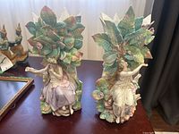 Pair of German porcelain vases with female figures and large leaves, one with repair visible