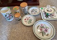 Overall view of Portmeirion Botanic Garden ceramic items including plates, canisters, utensil holder, tart stand, and plastic tray on carpeted floor.
