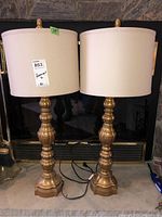 Two matching gold-toned table lamps with white drum shades, standing side by side showing overall wear and finish condition.