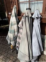 Four closed outdoor umbrellas leaning against a wooden structure outside showing different fabric colors and conditions.