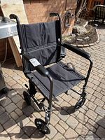 Side angle showing collapsible wheelchair, black fabric seat and backrest, padded armrest, and rear wheel lock lever