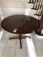 Round dark wood dining table shown from an angled top view in natural light, showing wood grain and condition of finish.