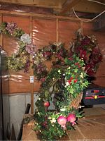 Four assorted faux flower wreaths hanging on a wooden wall, showing variety in flower types and colors including hydrangeas, roses, berries, and mixed foliage.
