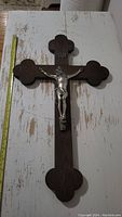 Overhead photo of vintage wooden crucifix with metal Jesus figure against white wood background, showing the full length with a measuring tape indicating about 20 inches tall.