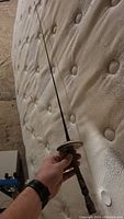 Photo showing the full length of the antique rapier sword held by a hand against a mattress background.