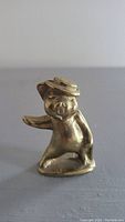 Small brass pig figurine standing upright and facing forward, wearing a tilted hat.