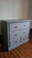Front and side angled view of the gray painted wooden dresser with three drawers and fluted side details.