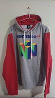 Grey hoodie with red sleeves hanging on a white hanger, showing front with Nintendo 64 logo and text.