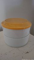 Stacked white porcelain cereal bowls with orange lids on top, showing product design and lid fit.