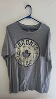 Full view of the grey Toronto Maple Leafs T-shirt hanging on a hanger showing the front print.