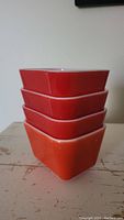 Stack of four red vintage Pyrex dishes nested together showing the shape and color.