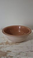 Side view showing the beige exterior and brown interior of the Pyrex bowl on a distressed wooden surface.