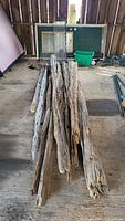 Photo showing a collection of weathered cedar fence pickets stacked together indoors against a wooden fence background. The pickets appear aged with visible cracks and surface wear.