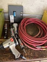 Overview of all pneumatic tools together with coiled red air hose on wooden workbench.