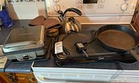 Photo showing Cuisinart waffle maker, Master Chef electric griddle, and Wagner cast iron skillet together on a stove top.