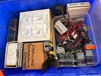Photo shows a plastic tote containing boxes labeled for relays and momentary switches, and loose wiring and electrical parts.