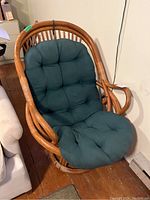 Front view of bamboo cane swivel rocking chair with dark green cushion, showing rounded armrests and padded seat.