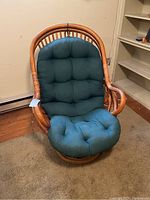 Front view of bamboo cane swivel rocking chair with original green tufted cushion, showing curved bamboo frame and cushion detail.
