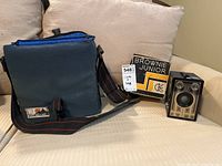 Vintage Kodak Brownie Junior camera with original box and blue camera bag placed on a white couch.