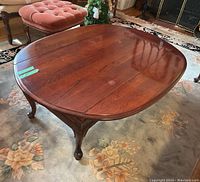 Oval wooden coffee table with drop leaf sides extended, showing wood grain and some finish flaws.