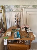 Wide view of wooden table displaying costume jewelry assortment and necklace holder with miniature dress form, various boxes and loose pieces scattered